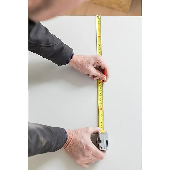 Stanley Kapselmaßband PowerLock - 5 m - Eine Person misst eine Oberfläche mit einem gelben Rollmaßband und markiert mit einem roten Stift die Messung.