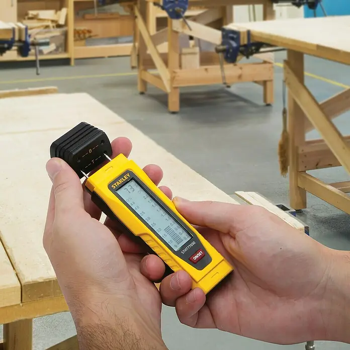 Stanley Feuchtigkeitsmessgerät - Geeignet für: Baumaterialien/Holz - Nahaufnahme eines gelben Stanley Feuchtigkeitsmessgeräts, das in einer Werkstatt Holz misst.