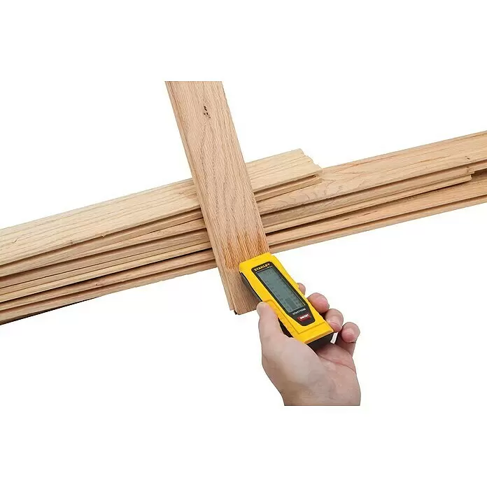 Stanley Feuchtigkeitsmessgerät - Geeignet für: Baumaterialien/Holz - Gelbes Stanley Feuchtigkeitsmessgerät in der Hand, misst Feuchtigkeit in einem Holzbrett aus einem Stapel.