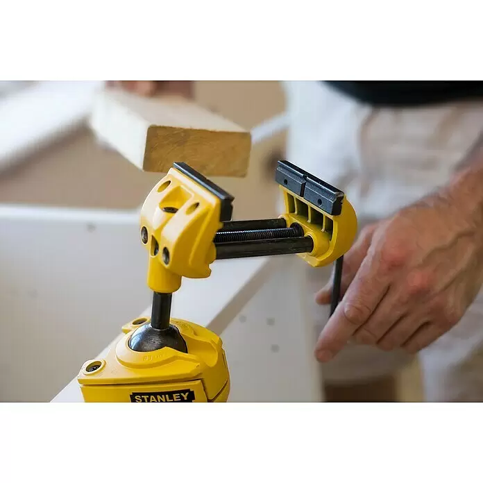 Stanley Schraubstock MaxSteel - Backenbreite: 70 mm - Gelber Stanley mobiler Werkstatt-Schraubstock spannt ein Holzstück, bedient von einer Hand.