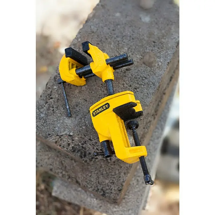 Stanley Schraubstock MaxSteel - Backenbreite: 70 mm - Nahaufnahme eines gelben Stanley-Universal-Mehrzweckschraubstocks, der auf einer Betonoberfläche steht und seine robuste Konstruktion hervorhebt.