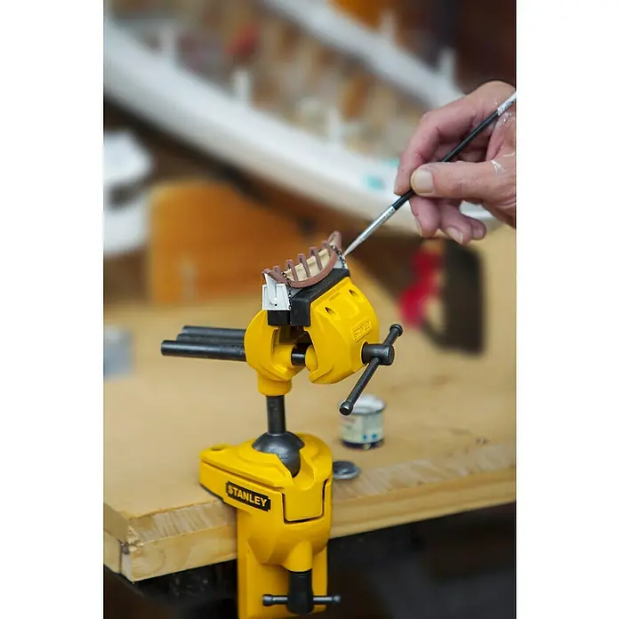 Stanley Schraubstock MaxSteel - Backenbreite: 70 mm - Nahaufnahme eines gelben Stanley-Schraubstocks, der ein Schiffsmodell hält, während eine Hand es mit einem Pinsel bemalt. Werkzeug für Modellbau.