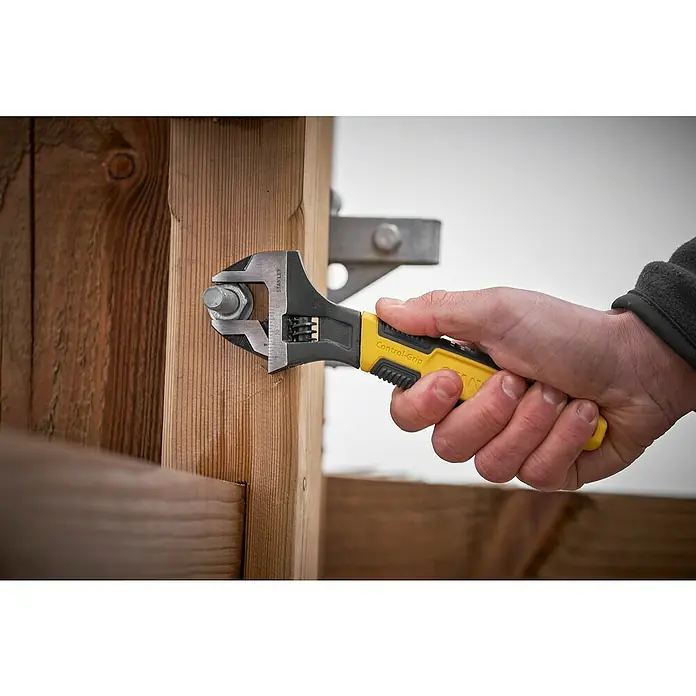 Stanley Rollgabelschlüssel MAXSTEEL™ - Schlüsselweite: 24 mm - Nahaufnahme eines Stanley Control-Grip-Schraubenschlüssels, der an einer Holzstruktur einen Bolzen festzieht. Das Werkzeug ist benutzerfreundlich.