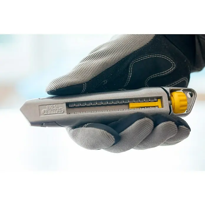 Stanley Cuttermesser - Klingenbreite: 18 mm - Nahaufnahme eines Handschuhs, der ein graues Stanley 10-018 Teppichmesser mit gelbem Schieber hält.