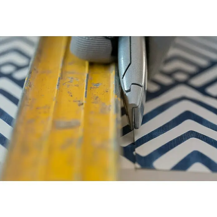 Stanley Cuttermesser - Klingenbreite: 18 mm - Nahaufnahme einer Metalleinhausung mit Abisolierzange, die auf einem Untergrund mit Chevron-Muster platziert ist.