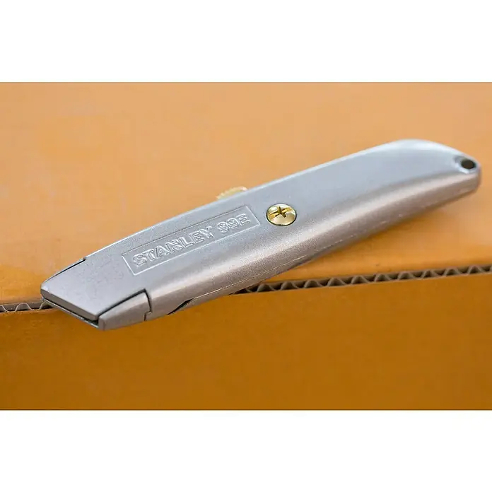 Stanley Schiebemesser 99E - Trapezklinge, Schiebbare Klinge - Nahaufnahme eines Stanley 99E Cuttermessers auf einem Karton, ein Werkzeug für präzise Schnitte und vielseitige Anwendungen im Alltag.