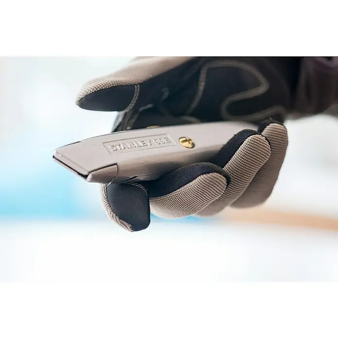 Stanley Schiebemesser 99E - Trapezklinge, Schiebbare Klinge - Nahaufnahme eines Arbeiters mit Handschuhen, der ein Stanley 99E Cuttermesser hält, wobei der Fokus auf dem Werkzeug und seiner Funktionalität liegt.