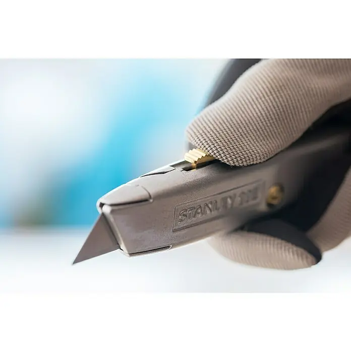 Stanley Schiebemesser 99E - Trapezklinge, Schiebbare Klinge - Nahaufnahme eines Stanley-Messers in einer Hand mit Handschuh, wobei der Fokus auf der scharfen Klinge und dem robusten Design liegt.