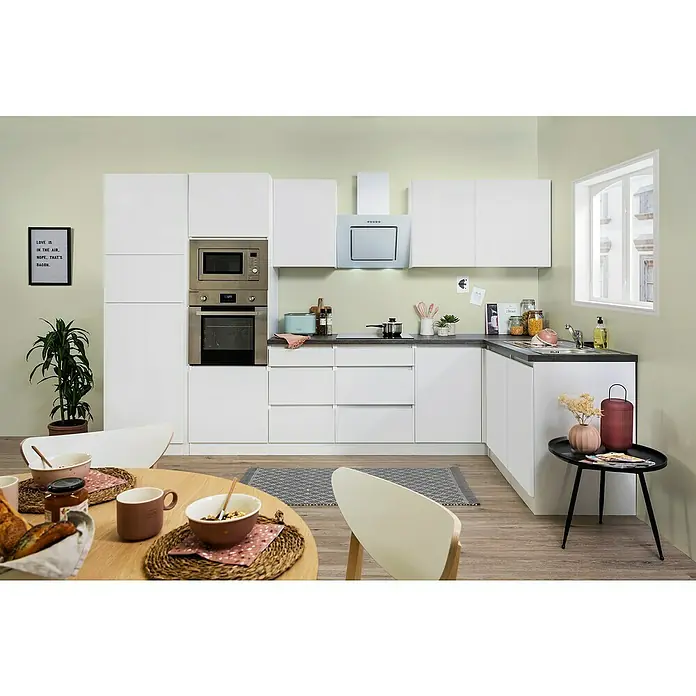 Respekta Premium Winkelküche Lorena - Breite: 345 cm, Weiß, Hochglänzend, Steinoptik, Mit Elektrogeräten - Helles Kücheninterieur mit modernen weißen Schränken, Geräten aus Edelstahl und einer gemütlichen Essecke mit Holztisch und Geschirr.