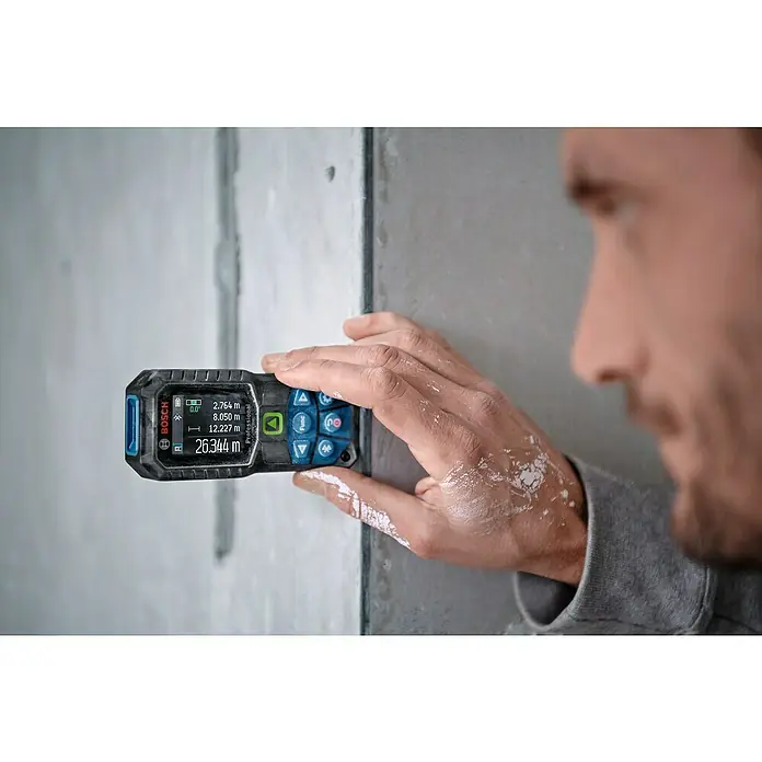 Bosch Professional Laserentfernungsmesser GLM 50-27 CG - Anzahl Akkus: Ohne Akku, Messbereich: 0,05 - 50 m - Nahaufnahme eines Bosch Professional Laser-Entfernungsmessers, der von einer Person an einer Wand gehalten wird, mit Anzeige verschiedener Messwerte.