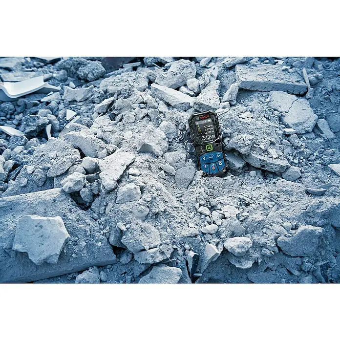 Bosch Professional Laserentfernungsmesser GLM 50-27 CG - Anzahl Akkus: Ohne Akku, Messbereich: 0,05 - 50 m - Der Bosch Professional GLM 50-27 CG Laserentfernungsmesser liegt auf einem Haufen Bauschutt. Zu sehen ist das große Farbdisplay und die blauen Tasten.