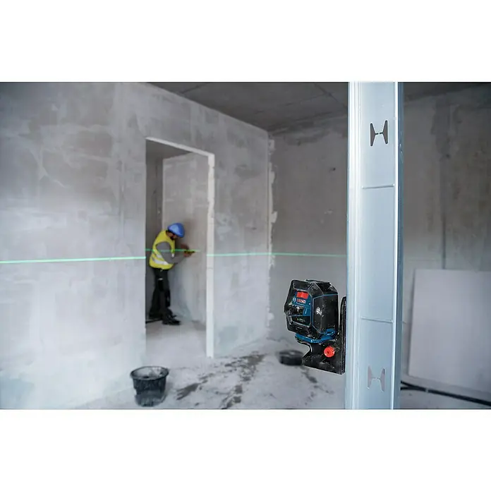Bosch Professional Kombilaser GCL 2-50 G mit Bosch Professional Stativ BT 150 - Arbeitsbereich: 50 m (mit Empfänger) - Ein Bosch Professional Laser-Nivelliergerät ist an einem Metallpfosten befestigt und projiziert einen grünen Laserstrahl in einem Rohbauraum.