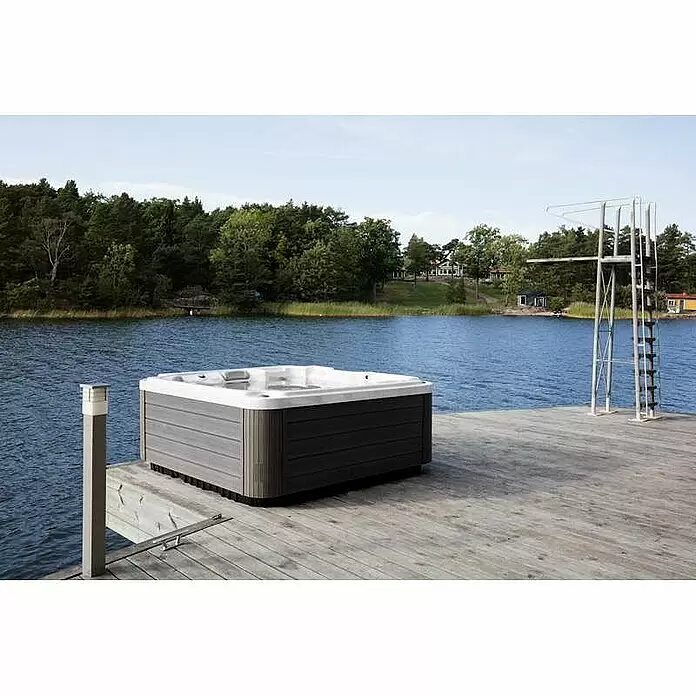 Camargue Außen-Whirlpool Serenity - 213 x 213 x 91 cm, Grau/Weiß, Max. Personenzahl: 6 - Grauer Whirlpool mit weißem Interieur auf einem Holzsteg an einem ruhigen See. Ein Sprungbrett steht in der Nähe.
