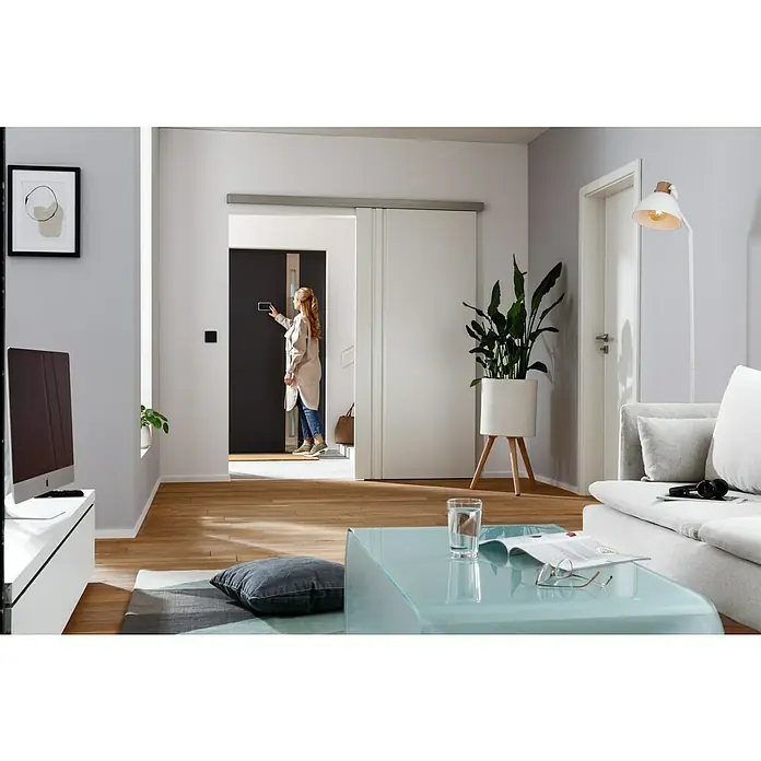 Kilsgaard Schiebetür-Komplettset 422-L - 935 x 2.050 mm, Weiß, Wabe - Moderne Wohnung mit Schiebetürsystem und einer Frau, die eine digitale Türklingel bedient, die das Zuhause intelligenter macht.