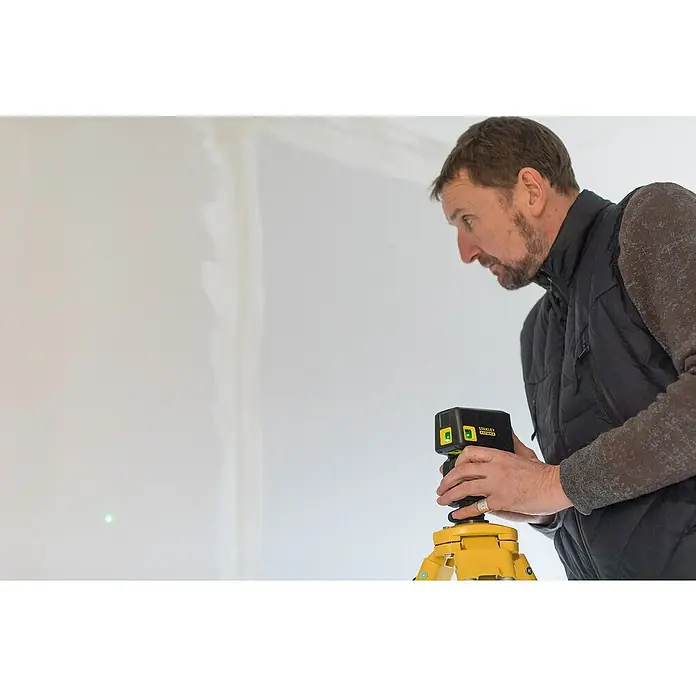 Stanley FatMax Punktlaser FMHT1-77437 - Max. Arbeitsbereich: 45 m, Stativ-Gewinde: ¼″ - Ein Mann justiert einen Stanley Fatmax Laser-Wasserwaage auf einem gelben Stativ, der einen grünen Laserpunkt an die Wand wirft.
