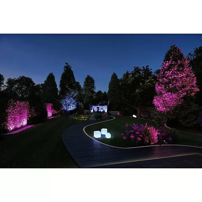 Paulmann Plug & Shine Basis-Set LED-Bodeneinbauleuchte Smart Home Zigbee - 3,6 W, Silber, Ø x H: 9,8 x 9,2 cm, Per App steuerbar, IP65 - Ein Gartenweg mit LED-Streifen, beleuchtet von farbigen Lichtern an Bäumen, Pflanzen und Dekowürfeln bei Nacht.