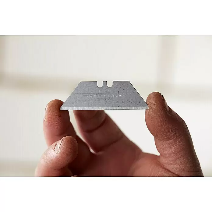 Stanley Ersatzklingen - 10 Stk. - Metallisch graue Teppichmesserklinge, von zwei Fingern gehalten, zeigt scharfe Kante und „Stanley“-Markierung.