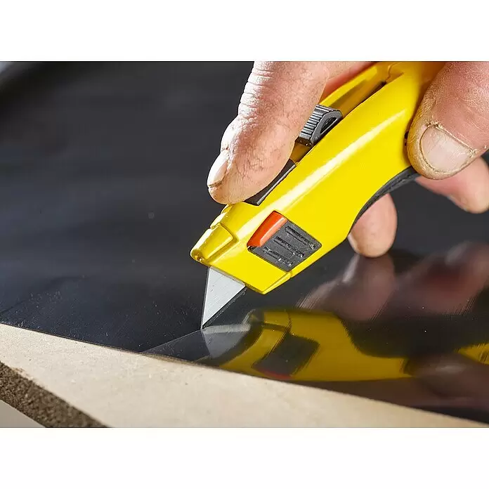 Stanley Ersatzklingen - 10 Stk. - Hand schneidet schwarzes Material mit gelbem Teppichmesser auf Holz.
