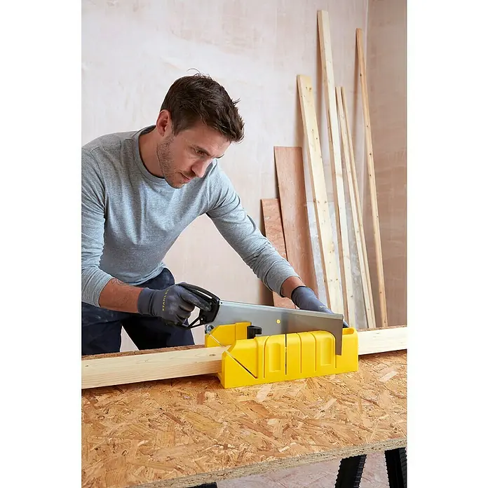 Stanley Gehrungsschneidladen-Set - Blattlänge: 355 mm, 317,5 x 170,2 x 108,3 mm - Ein Mann sägt Holz mit einer Handsäge und einer gelben Gehrungslade. Das Werkzeug ermöglicht präzise Schnitte für Holzbearbeitungsprojekte.