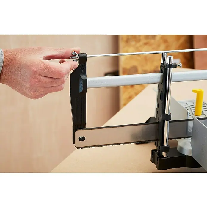 Stanley Gehrungslade 1-20-800 mit Säge - L x B x H: 560 x 143 x 95 mm - Detailaufnahme einer Handsäge beim Festziehen der Flügelschraube. Das Werkzeug ist ideal für präzise Schnitte und Heimwerkerarbeiten.