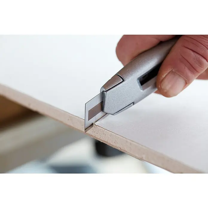 Stanley Abbrechklinge Carbide - 50 Stk. - Ein scharfes Cuttermesser schneidet präzise durch eine weiße Gipskartonplatte, ideal für saubere Schnitte bei Bauarbeiten.