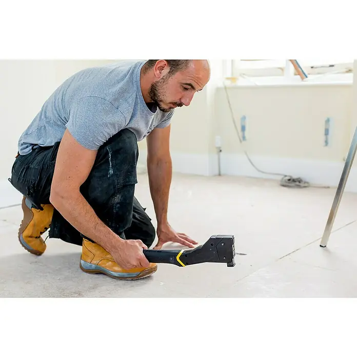 Stanley FatMax Hammertacker FMHT81394-9 - Wiederbefüllbar - Ein Mann auf den Knien, der ein schwarzes und gelbes Teppichverlegewerkzeug hält, um Teppich zu verlegen.