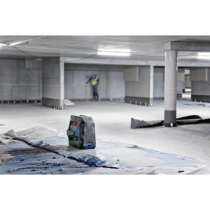 Bosch Professional Láser combinado GCL 2-50 - Zona de trabajo: 50 m (con receptor) - Un nivel láser Bosch Professional proyecta una línea láser verde en un edificio en construcción mientras un trabajador toma medidas.