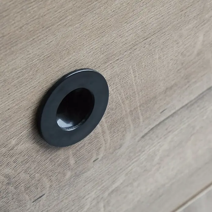 Muebles Pitarch Camila Cabecero de cama con mesita - 2 pzs., Roble gold - Primer plano de un tirador de mueble redondo y negro, empotrado en una superficie de madera clara, que muestra su diseño elegante y moderno.