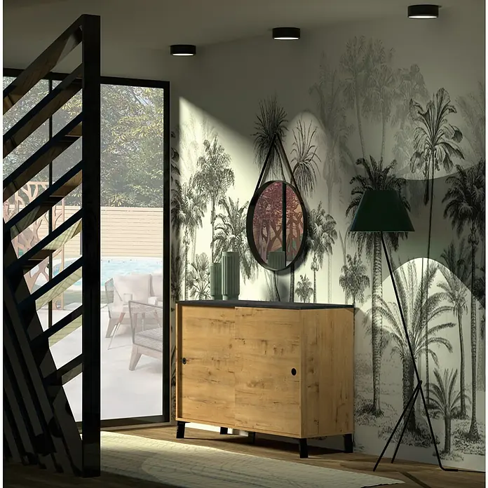 Muebles Pitarch Kamet Aparador - L x An x Al: 40 x 120 x 87 cm, Roble Gold/Negro - Escena interior con un mueble de madera con puertas correderas, un espejo y una lámpara de pie contra una pared con diseño de palmeras.