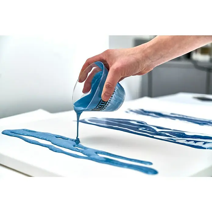 Liquitex Professional Gießmedium Gloss - 473 ml, Transparent - Hand gießt blaue Flüssigfarbe aus einem Messbecher auf eine Leinwand, um ein abstraktes Kunstwerk zu schaffen. Die Farbe fließt in dicken Strähnen.