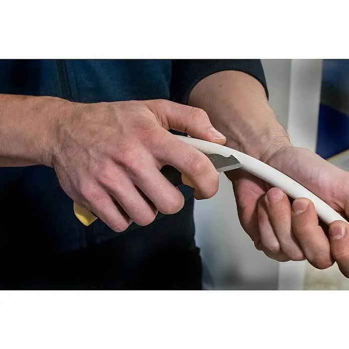 Morakniv Elektrikermesser - Klingenlänge: 21 mm, Klingenbreite: 18 mm - Eine Nahaufnahme einer Person, die ein weißes Rohr mit einem gelben Universalmesser schneidet, wobei der Fokus auf der Schnittstelle liegt.