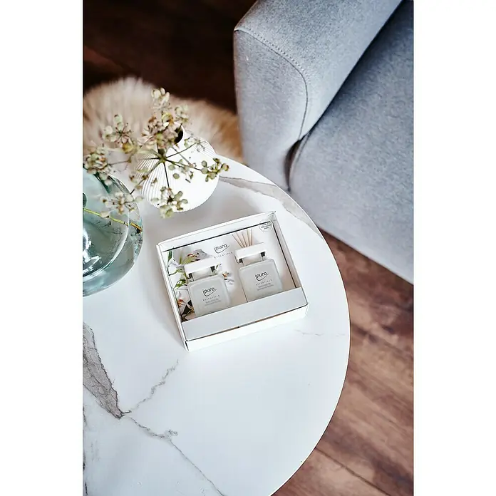 Ipuro Essentials RaumduftWhite Lily, 2 Stk., 50 ml - Ein stilvolles Bild zeigt ein Puro Essentials Duftset auf einem Marmortisch neben Vasen und einem grauen Sessel. Elegante Atmosphäre.