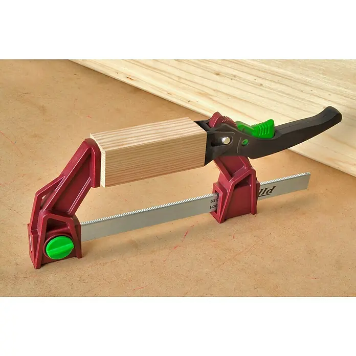 Piher Tornillo de apriete monomanual Light Pal - Anchura de sujeción: 300 mm, Fuerza de tensión: 1.177 N - Primer plano de una pinza de palanca roja que sujeta un trozo de madera, colocada sobre un banco de trabajo.