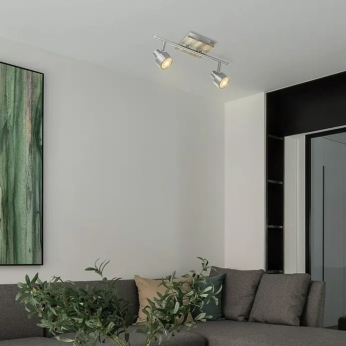 Home Sweet Home LED-Deckenstrahler Drift - 5,8 W, L x B x H: 12 x 35,5 x 17,5 cm, Holz/Silber, Warmweiß, 2 Stk. - Deckenstrahler mit zwei Lampen. Die Leuchte ist silberfarben und spendet warmes Licht im Raum, der mit einem grauen Sofa ausgestattet ist.