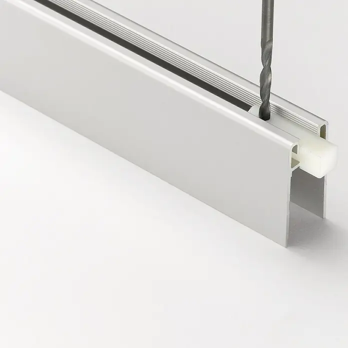 Room Plaza Easy Sockelprofil - Passend für: Room Plaza Easy Schiebetür-Bau-Sets, 1.200 mm, Silber - Nahaufnahme einer Aluminiumleiste, in die mit einem Bohrer ein Loch gebohrt wird, was die Bearbeitung und Anpassung des Materials zeigt.