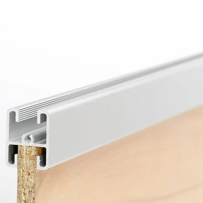 Room Plaza Easy Kranzprofil - Passend für: Room Plaza Easy Schiebetür-Bau-Sets, 1.200 mm, Silber - Nahaufnahme einer weißen Aluminiumprofilleiste, die an einer Holzplatte befestigt ist, ideal für Möbelbau und Innenausbau.