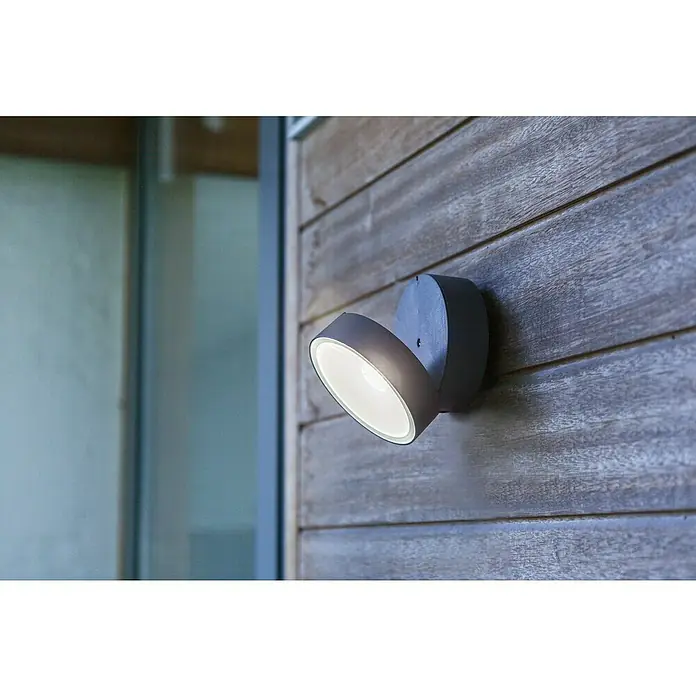 Lutec LED-Außenwandleuchte - 6,7 W, Anthrazit - Nahaufnahme einer modernen Außenwandleuchte aus Metall, die an einer Holzfassade befestigt ist und helles Licht abstrahlt.