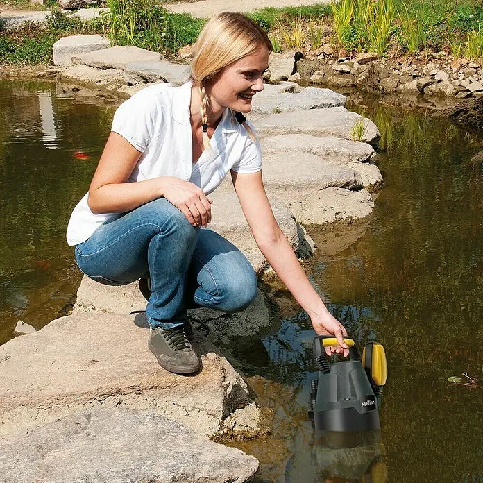 Neptun Schmutzwasserpumpe NSP-E 33 - 330 W, Max. Fördermenge: 9.500 l/h, Eintauchtiefe: 7 m - Eine Frau benutzt eine NEPTUN-Teichpumpe, um das Wasser in einem kleinen Teich zu reinigen. Die Pumpe ist schwarz und gelb.