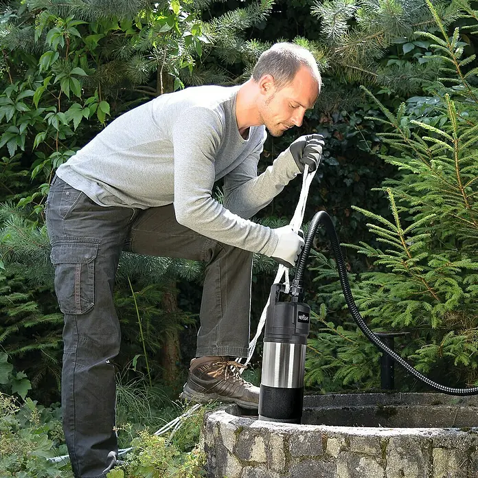 Neptun Drucktauchpumpe NTP-E 110 AUTOMATIC - 1.100 W, Max. Fördermenge: 6.000 l/h - Ein Mann bedient eine Neptun-Tauchpumpe in einem steinernen Brunnen, umgeben von üppigem Grün.