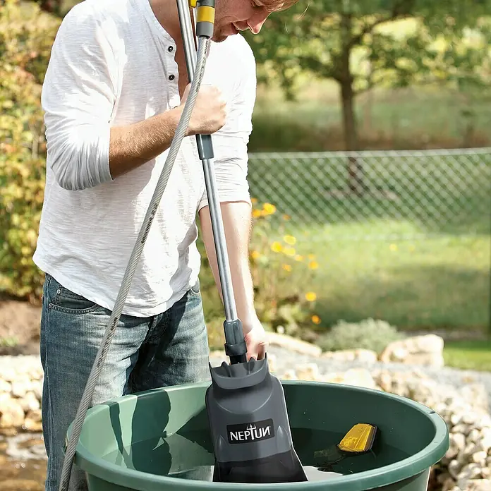Neptun Regenfasspumpe NRP-E 40 - 400 W, Max. Fördermenge: 4.200 l/h - Ein Mann benutzt eine Neptun-Teichschlammsauger in einem grünen Behälter, um Schlamm aus dem Teich zu entfernen.