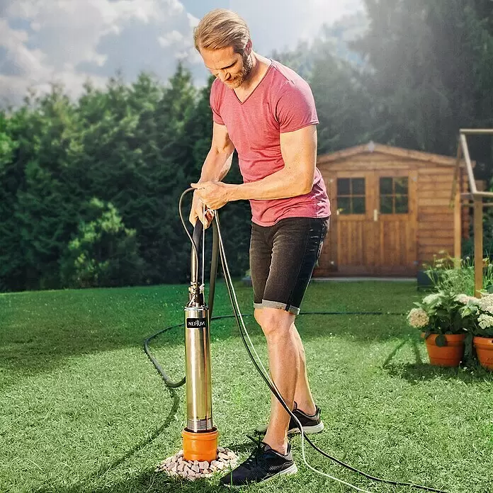 Neptun Tiefbrunnenpumpe NTP-E 100 - 1.000 W, Max. Fördermenge: 6.500 l/h - Mann installiert eine Edelstahl-Tauchpumpe mit orangefarbenem Sockel im Garten.