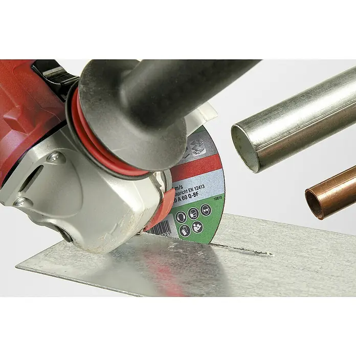 KWB Disco de corte - Ø x Es: 150 x 1,2 mm, Orificio: 22,23 mm - Una amoladora angular roja y plateada corta una lámina de metal con un disco de corte verde, mientras que hay tuberías al fondo.