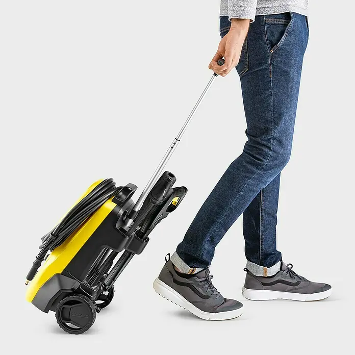 Kärcher Hidrolimpiadora de alta presión K4 Compact UM - 130 bar, 1.800 W, Capacidad de bombeo: 420 l/h - Un hombre tira de una hidrolimpiadora Kärcher amarilla con asa telescópica para facilitar su transporte.