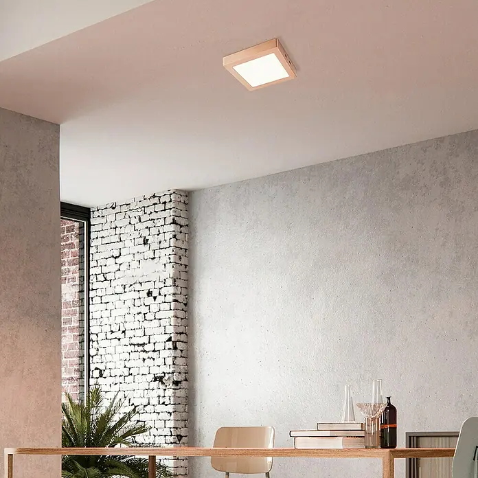 Home Sweet Home LED-Deckenleuchte Ska - 15 W, L x B x H: 22,5 x 22,5 x 4 cm, Kupfer, Warmweiß - Eine quadratische Deckenleuchte aus Holz strahlt helles Licht in einem modernen Raum mit Betonwand und Ziegelsteinakzenten aus.