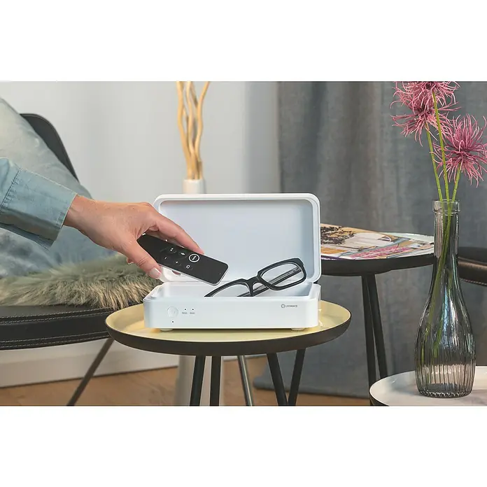 Ledvance Desinfektionsbox UVC LED - Weiß, 21,9 x 12,6 x 6,3 cm, USB-Anschluss - Eine Hand legt eine schwarze Fernbedienung in eine weiße LEDVANCE UV-Reinigungsbox, in der sich eine Brille befindet.