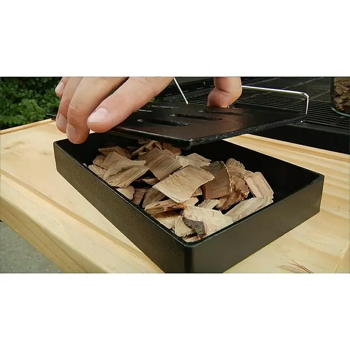 Char-Broil Räucherbox - L x B x H: 20,5 x 12,8 x 3,5 cm - Ein Mann öffnet eine Räucherbox voll mit Holzspänen. Perfekt für das Räuchern auf dem Grill, um köstliche Aromen zu erzeugen.