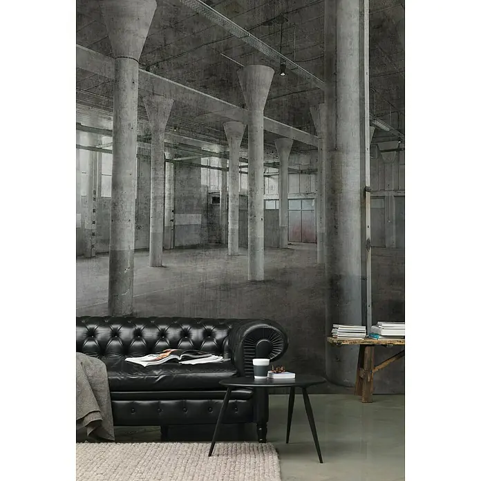 Rasch Factory 4 Fototapete Digitaldruck - 250 x 300 cm - Ein elegantes Wohnzimmer mit schwarzem Ledersofa und kleinem Beistelltisch, vor einer industriellen Betonwand, wirkt stilvoll.