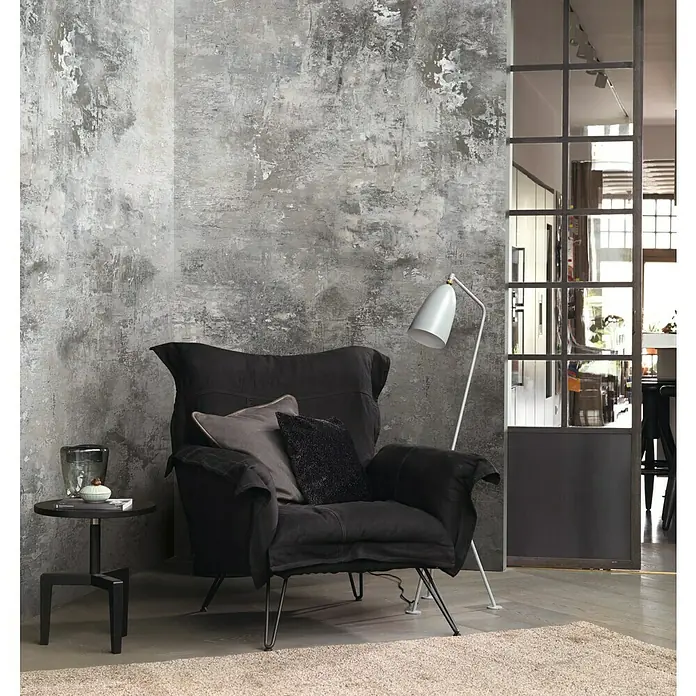 Rasch Factory 4 Fototapete Digitaldruck - 212 x 300 cm, Grau - Gemütlicher Lesesessel in Schwarz mit Kissen und Stehlampe neben einem kleinen Tisch mit Dekoration vor einer grauen Wand.
