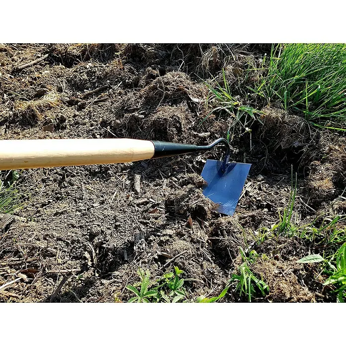 Azada - Anchura de trabajo: 12 cm, Acero - Primer plano de una azada con mango de madera clavada en tierra suelta con escasos grupos de hierba, ideal para jardinería y deshierbe.