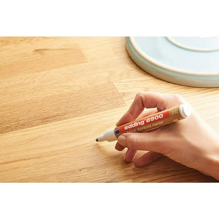 Edding Marcador permanente para muebles - Pino - Se está usando un rotulador para muebles Edding 8900 para reparar rasguños en una superficie de madera, con un tazón azul al fondo.